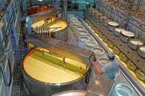 GRUYERE, SWITZERLAND - DECEMBER 31, 2014: Worker of the cheese-making factory of Gruyeres checking the temperature in the vats with milk